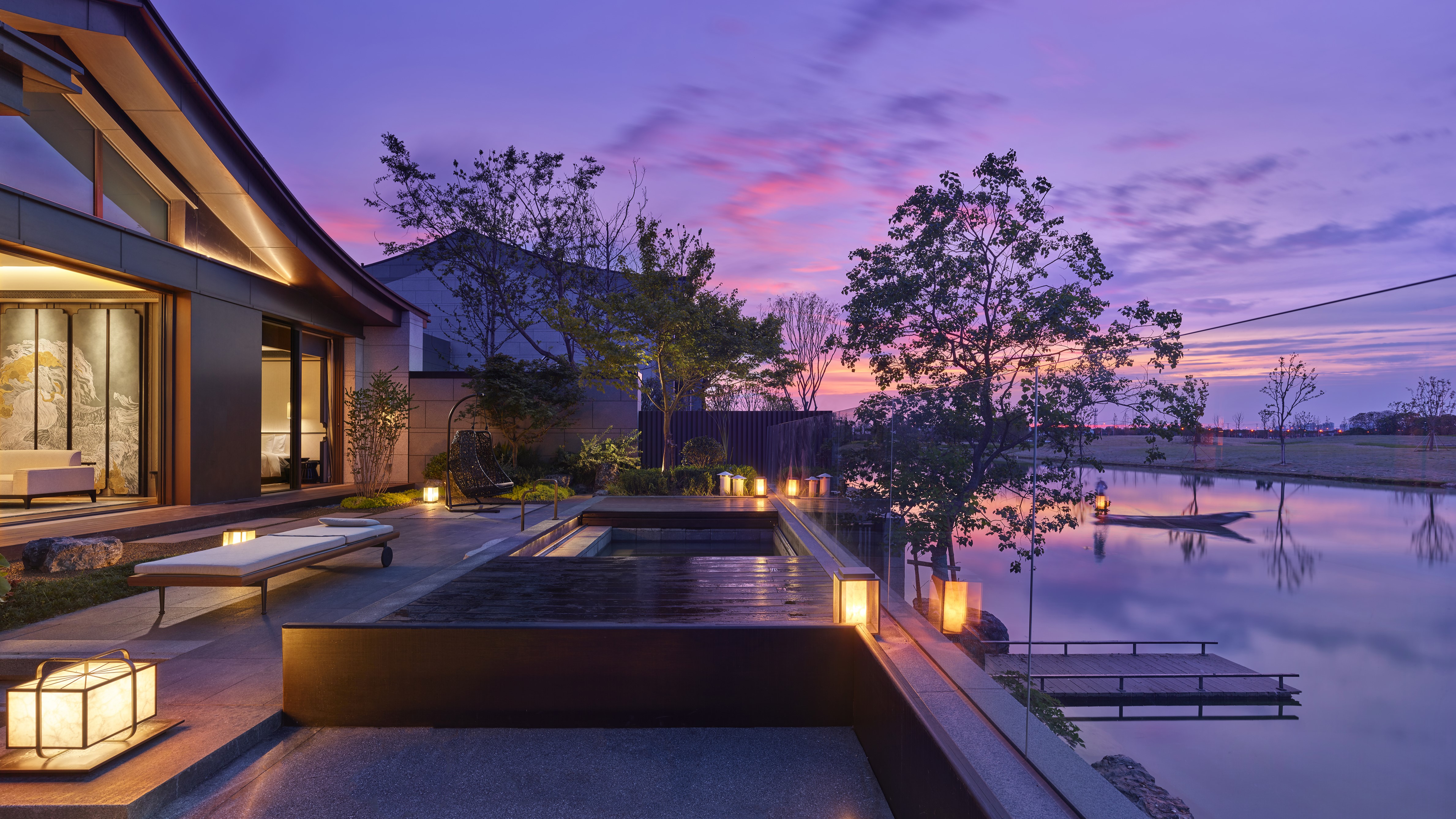 Banyan Tree Yangcheng Lake villa terrace with glowing lanterns beside a tranquil lakeside at sunset.
